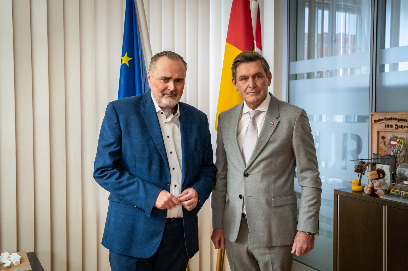 Landeshauptmann Hans Peter Doskozil und Mobilitätsminister Peter Hanke stehen nebeneinander in einem Büro vor der EU- und der Burgenland-Fahne